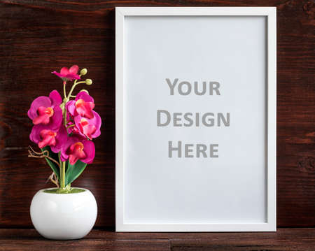 White vertical picture frame and artificial flower decoration on a dark wooden shelf. Clipping path for a frameの写真素材