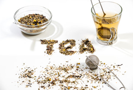 Tea text made by tea leaf on wwhite background surface with a bowl of tea and small glass tea cupの写真素材