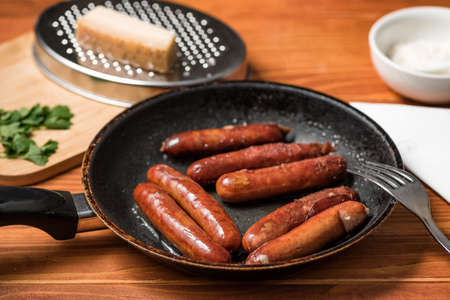 Tasty fried sausages in frying pan with Parmigiano and parsley, over wooden backgroundの写真素材