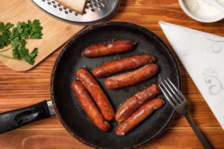 Tasty fried sausages in frying pan with Parmigiano and parsley, over wooden background. Top viewの写真素材