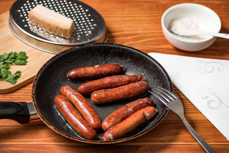 Tasty fried sausages in frying pan with Parmigiano and parsley, over wooden backgroundの写真素材