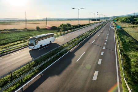 Modern White bus traveling on a wide highway in a rural backdrop. Highway transportation of passengers in a bus line.の写真素材