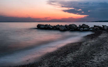 Tropical beach on beautiful sunset. Nature seascape background. Sun setting in waves of Aegean sea in Greeceの写真素材