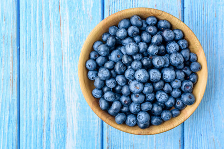 Fresh blueberries in a wooden bowl on an old blue wooden table. Healthy and dietary food concept. Blueberry is an antioxidantの写真素材