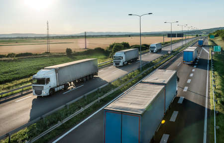 Transportation trucks in line passing on a highway on a bright blue day. Highway transit transportation with lorry trucks. Transportation And Trucking Industry.の写真素材