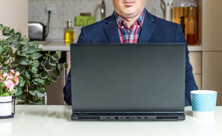 Trendy Mature man working from home with laptop sitting at the table in his kitchen, dressed in Suit. Home office conceptsの写真素材
