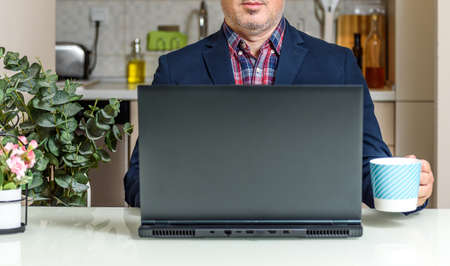 Trendy Mature man working from home with laptop sitting at the table in his kitchen, dressed in Suit. Home office conceptsの写真素材