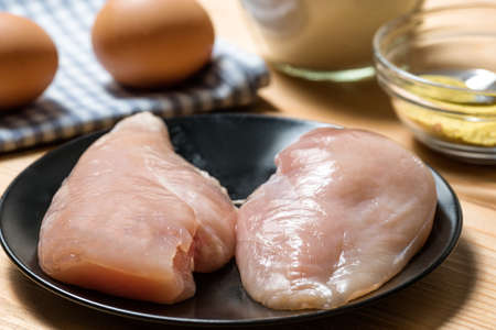 Chicken fillet on a cutting board ready for grilling, selective focus. Raw chicken breast with grill pan, flour and spices. Chicken steaks for cookingの写真素材