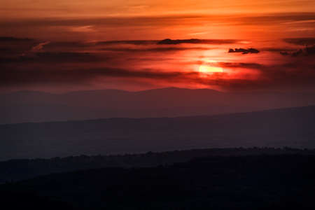 Sunset with layers of hills and mountains, soft focus. Mountain layers in sunset. Blue mountains and last sun lights landscape.の写真素材