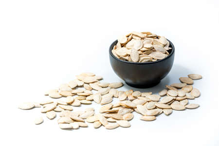 Pumpkin seeds in a bowl isolated on white background with some seeds spilled around. Roasted and salted pumpkin seeds for snacksの写真素材
