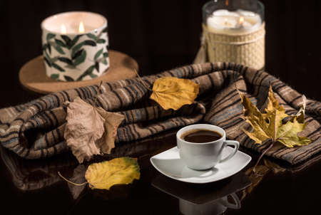 Autumn coffee scene. A cup of coffee on a dark glass table and a warm scarf on a background of...