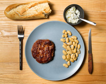Tasty grilled burger served with coocked vegetarian beans in a plate on a rustic wooden table. Flat lay, top viewの写真素材