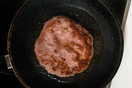 Meat burger being shallow fried in oil on a frying pan, close up. Top view. Flat lay.
