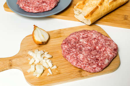 Raw minced meat burgers with onion and spices on white table or board for background. Selective focus. Raw meat hamburger with fresh onion on a wooden board ready to fryの写真素材