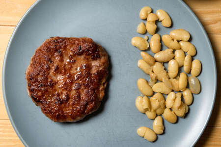Tasty grilled burger served with coocked vegetarian beans in a plate on a rustic wooden table. Flat lay, top viewの写真素材
