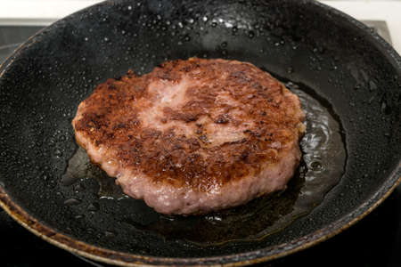 Meat burger being shallow fried in oil on a frying pan, close up, selective focusの写真素材