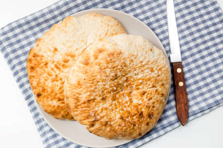 Loafs of flat round wheat bread in a plate, on a blue kitchen cloth over white tableの写真素材