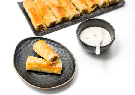 Meat rolls pastry - fried minced pork meat in spring rolls in a black oval plate, isolated on white background with stacks of rolls. Selective focus. Top Viewの写真素材