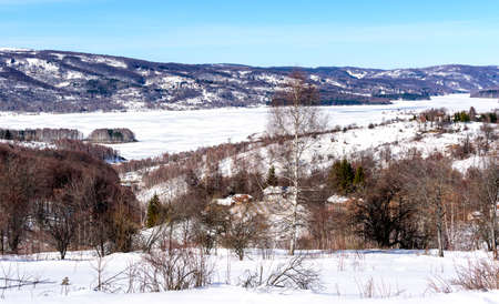 Winter landscape by the frozen lake with hills in the background background. Frozen Lake on a cold winter dayの写真素材