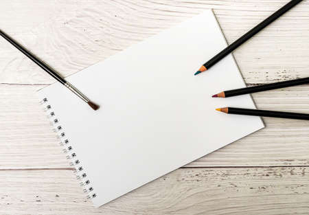 Notebook with white sheets and colored pencils for drawing on white wooden backgroundの写真素材