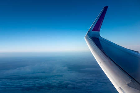 Wing of an airplane above the clouds. The view from the airplane window to the clouds and sunset. Airplane wing above thick white clouds. Wonderful breathtaking view.の写真素材