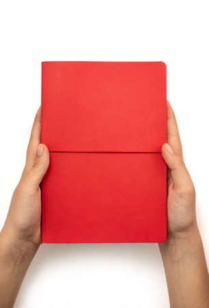 Female hands holding red book with blank cover on white background, top viewの写真素材