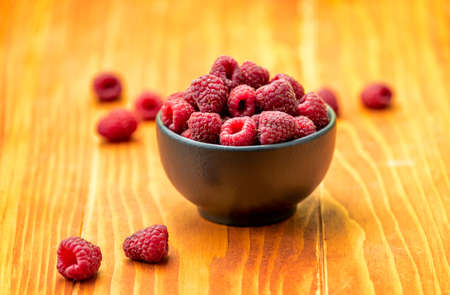 Ripe sweet raspberries in bowl on wooden tableの写真素材