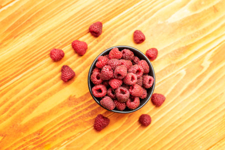 Ripe sweet raspberries in bowl on wooden table. Top View