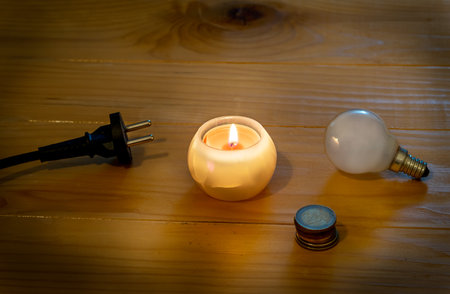 Saving electricity concept. Electric bulb and cable plug with candle on a wooden table. Eugo coins. Symbol of return to the past. Incandescent bulb and candle. Power cut or power oの写真素材