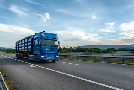 Big blue truck driving on the highway through forested landscape at sunset.の写真素材