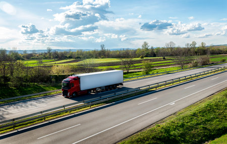 Highway scene with Red lorry truck with white trailer passing on a highway driving at beautiful dramatic sunset. Transportation vehicleの写真素材
