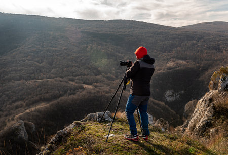 Photographer taking photographs with digital camera on a tripod in mountains. Travel and active lifestyle conceptの写真素材