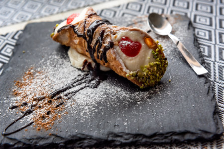 Italian Sicilian cannolo pastry dessert closeup on black stone plate macro with texture of yellow crust and ricotta cheese and pistachio cream filling with chocolate chips in cannoの写真素材