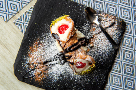 Italian Sicilian cannolo pastry dessert closeup on black stone plate macro with texture of yellow crust and ricotta cheese and pistachio cream filling with chocolate chips in cannoの写真素材