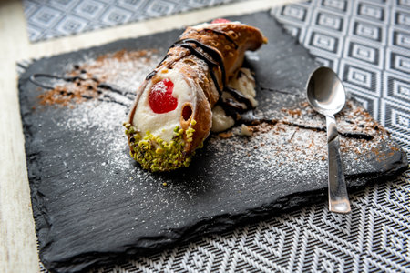 Italian Sicilian cannolo pastry dessert closeup on black stone plate macro with texture of yellow crust and ricotta cheese and pistachio cream filling with chocolate chips in cannoの写真素材