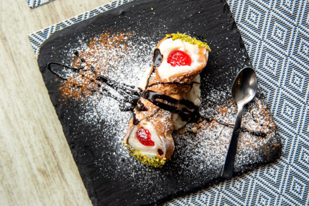 Italian Sicilian cannolo pastry dessert closeup on black stone plate macro with texture of yellow crust and ricotta cheese and pistachio cream filling with chocolate chips in cannoの写真素材