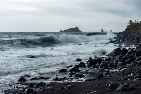 Waves hitting the shore on a cloudy overcast rainy stormy day. Cyclops Coast, black volcanic rocks and send on Sicily, near the town of Acirealeの写真素材