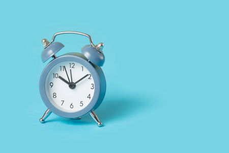 Close up one small blue metal twin bell retro alarm clock over light blue background with copy space, low angle front viewの写真素材