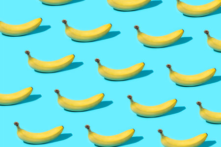 Trendy Summer food pattern made with yellow bananas on bright light blue background. Minimal summer concept.の写真素材