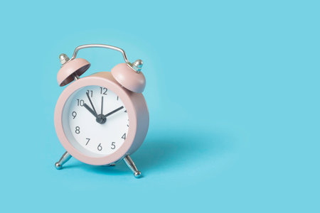 Close up one small pink metal twin bell retro alarm clock over light blue background with copy space, low angle front viewの写真素材