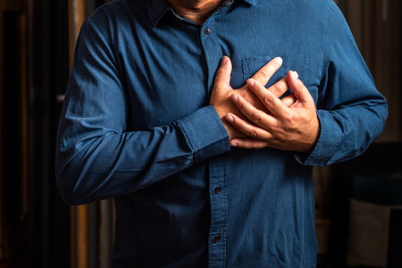 Heart attack. Man in blue shirt clutching his chest from acute pain. Heart attack symptom. Severe heartache, man suffering from chest pain, having heart attack or painful cramps, pの写真素材