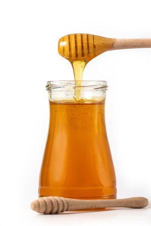 Honey drips from a spoon into a jar on white backgroundの写真素材