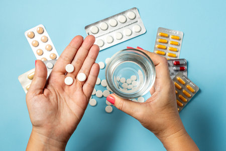 Hand Holding Colorful Pills With Glass Of Clear Water Over Blue Backgroundの写真素材