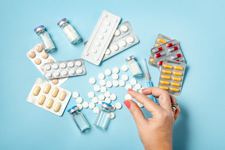 Hand holding one white pill on blue background full of colorful pills and medicinesの写真素材