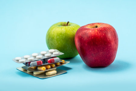 Pills capsules of medicament isolated on blue background with red and green applesの写真素材