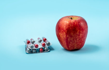 Pills capsules of medicament isolated on blue background versus red apple. Concepto of medicaments and healthの写真素材