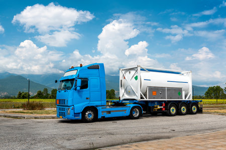 Truck with tank trailer parked near highway with countryside backdrop and a blue sky with white cloudsの写真素材