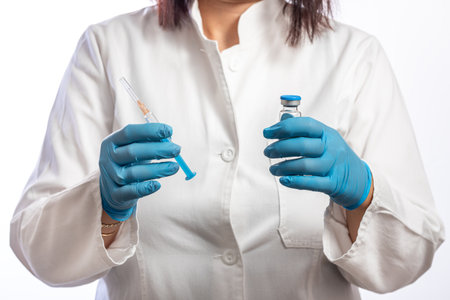 Female doctor wearing white coat and blue protective gloves holding syringe and medicine or vaccine bottle. The concept of injection treatmentの写真素材