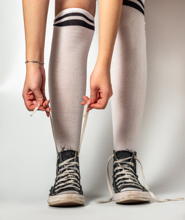 Girls hands tying laces on Old blue sneakers hipster style on girl legs in over the knee socks, on a...