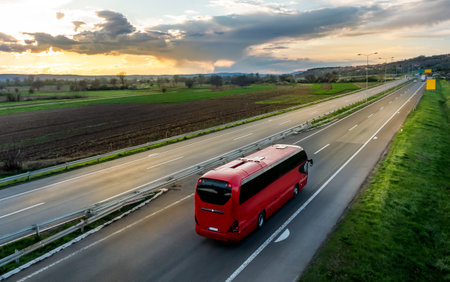 Red Modern comfortable tourist bus driving through highway at bright sunny sunset. Travel and coach tourism concept. Trip and journey by vehicleの写真素材